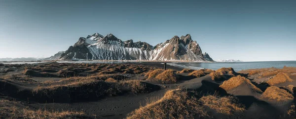 Young man tourist standing at beach during sunset runrise and gorgeous reflection of Vestrahorn mountain on Stokksnes cape in Iceland. Beautiful snow covered mountains. Location: Stokksnes cape — Stock Fotó