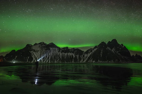 Jonge reiziger staan in de voorkant van Vestrahorn Stockknes bergketen met aurora borealis en reflectie op het strand in IJsland. Een van de mooiste natuurmonumenten van IJsland. — Stockfoto