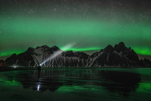 Νεαρός ταξιδιώτης στέκεται μπροστά από Vestrahorn Stockknes οροσειρά με Βόρειο Σέλας και αντανάκλαση στην παραλία στην Ισλανδία. Μια από τις πιο όμορφες διάσημη κληρονομιά της φύσης στην Ισλανδία. — Φωτογραφία Αρχείου