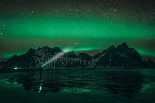 Young traveler standin in front of Vestrahorn Stockknes mountain range with aurora borealis and reflection at the beach in Iceland. One of the most beautiful famous nature heritage in Iceland. — Fotografia de Stock