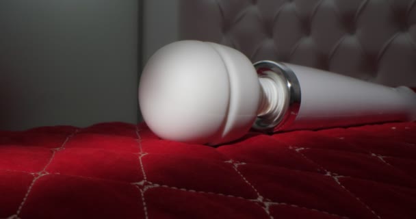 Detailed, extreme close-up of a white vibrator on a bed with carriage tie on a red blanket — Stock video