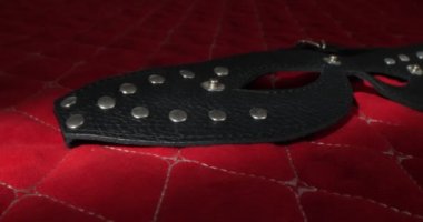 detailed, extreme close-up of a black leather eye mask on a red blanket