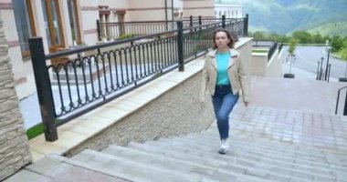 a woman in a white leather jacket and jeans climbs up the stairs on the street street