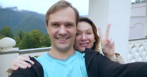 Happy couple man and woman greet and take a selfie against the backdrop of the landscape of a mountain resort and funicular — стоковое видео
