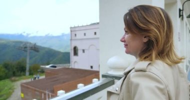 a woman in a white leather jacket is watching the movement of the funicular enjoying the scenery in a mountain resort