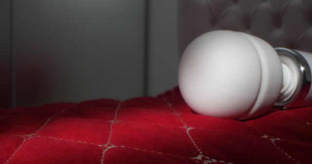 Detailed, extreme close-up of a white vibrator on a bed with carriage tie on a red blanket — Stock video
