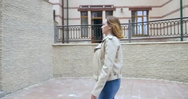 A woman in a white leather jacket and jeans climbs up the stairs on the street street — Stockvideo