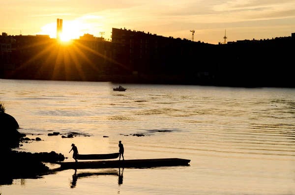 Silhueta de um jovem transportando canoa longe do lago ao pôr do sol — Fotografia de Stock