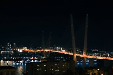 Golden Horn körfezi üzerindeki Vladivostok Altın Köprüsü. Ufuk çizgisi gece görüşü şehrin ışıklarıyla aydınlanıyor.