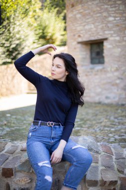 Eski taş binanın yanında kot pantolonlu, koyu renk saçlı genç Avrupalı kız.