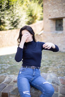 Dışarıda kotlu siyah saçlı genç Avrupalı kız elini yüzünü kapattı.