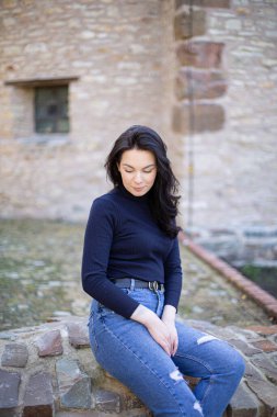 Kot pantolonlu, siyah saçlı, gözleri aşağıda genç bir kız.