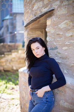 Duvarın yanındaki kot pantolonlu, lacivert kazaklı Avrupalı genç kız.