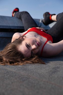 Beyaz Avrupalı kadın, koyu saçlı çatıda yatıyor, arkasında açık gökyüzü var.