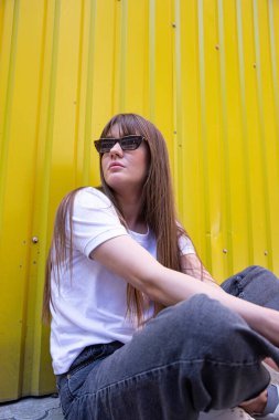 Koyu saçlı, kısmen sarı arka planda oturan beyaz kadın.