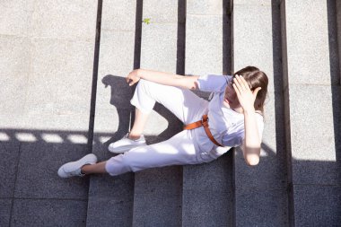 Güneşten saklanan uzun saçlı beyaz kız merdivenlerde oturuyor.