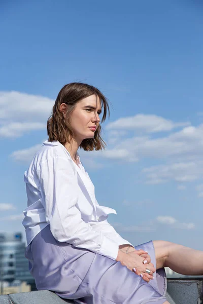 屋根の上に青い空の後ろに座っている若いヨーロッパの女性 — ストック写真