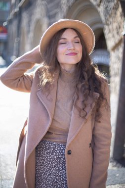 Kıvırcık saçlı, pastel pembeli, arkası kemerli, şapkasını tutan güzel bir kadın.