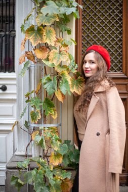 Eski kapının yanında kırmızı Fransız bereli, kıvırcık saçlı ve neredeyse sararmış üzümlü güzel bir kadın.