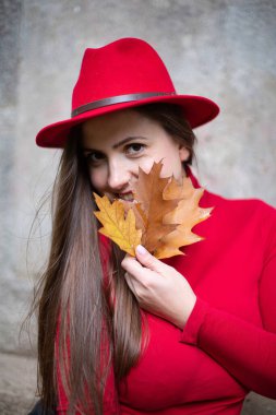 Uzun siyah saçlı, taş duvarın yanında parlak kırmızı saçlı, elinde sonbahar yaprakları tutan beyaz kadın portresi.