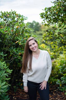 Ağaçların arasında beyaz süveter giyen gülümseyen Avrupalı kadın