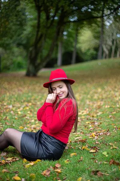 秋天公园的草地上坐着一头乌黑的长发 红得发亮的白人妇女 — 图库照片