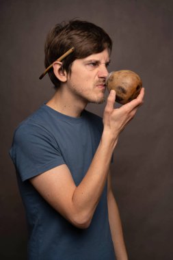 Genç yakışıklı, uzun, zayıf, beyaz, kahverengi saçlı, mavi gömlekli, gri arka planda mat bardağı kokan adam.