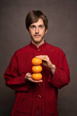 Genç, yakışıklı, zayıf, beyaz, kahverengi saçlı, gri arka planda turuncu gömlekli adam.