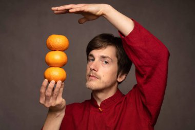 Yakışıklı, uzun boylu, zayıf, kahverengi saçlı, gri arka planda kırmızı gömlekli, portakallı bir adam.