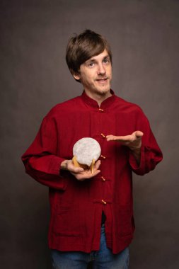 Genç, uzun boylu, zayıf, kahverengi saçlı, gri arka planda kırmızı tişörtlü, pu erh çay keki sunan beyaz adam.
