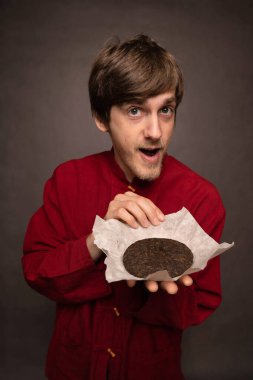 Kahverengi saçlı, uzun boylu, zayıf beyaz adam gri arka planda kırmızı gömlekli, pu erh çaylı kek açtı.