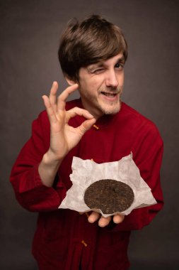 Genç yakışıklı, uzun, zayıf, kahverengi saçlı, iyi durumda. Gri arka planda kırmızı gömlekli, kakalı çay pastası tutan bir tabela var.