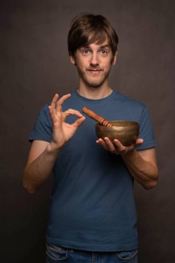 Genç yakışıklı, uzun boylu, zayıf, kahverengi saçlı, yeşil arka planda Tibet şarkı söyleyen, mavi tişörtlü, tamam işareti yapan beyaz adam.