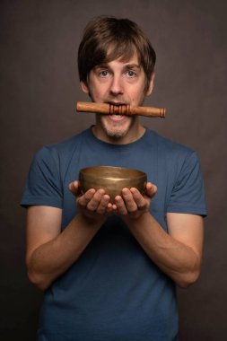 Genç yakışıklı, uzun boylu, zayıf, kahverengi saçlı, gri arka planda mavi gömlekli, Tibet çanağı tutan beyaz adam.