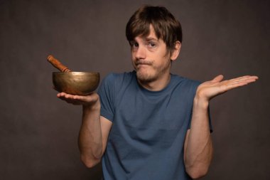 Genç yakışıklı, uzun boylu, zayıf, kahverengi saçlı, cahil, gri arka planda mavi tişörtlü Tibet şarkıcısı.