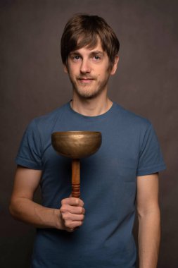 Genç yakışıklı, uzun boylu, zayıf, kahverengi saçlı, gri arka planda Tibet şarkı kasesini dengeleyen beyaz adam.