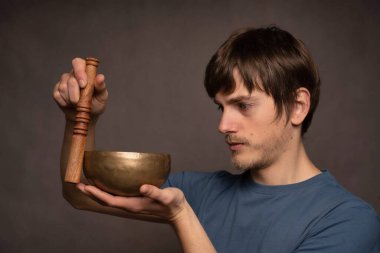 Genç yakışıklı, uzun boylu, zayıf, kahverengi saçlı, tuhaf görünüşlü, gri arka planda mavi tişörtlü Tibet şarkıcısı.