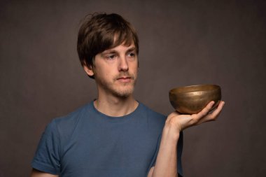 Genç yakışıklı, uzun boylu, zayıf, kahverengi saçlı, gri arka planda mavi gömlekli, düşünceli, beyaz bir adam.