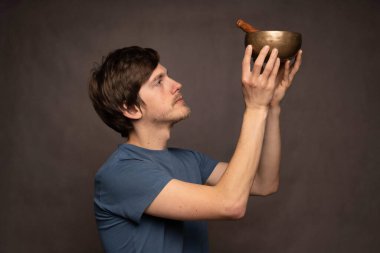 Genç yakışıklı, uzun boylu, zayıf, kahverengi saçlı, gri arka planda mavi gömlekli Tibet şarkıcılarına tapan beyaz adam.