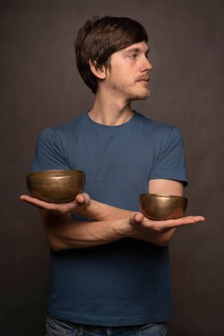 Genç yakışıklı, uzun, zayıf, kahverengi saçlı, gri arka planda mavi gömlekli, iki kase kollu beyaz adam.