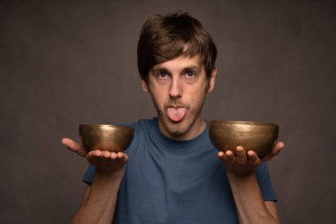 Genç yakışıklı, uzun boylu, zayıf, kahverengi saçlı, gri arka planda mavi gömlekli, kâseli, beyaz bir adam.