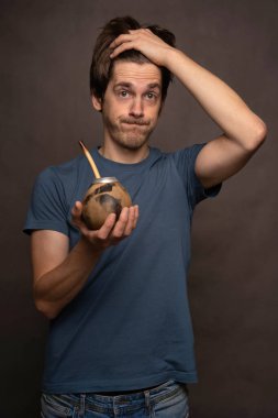 Genç yakışıklı, uzun, zayıf, kahverengi saçlı, gri arka planda mavi gömlekli, endişeli beyaz bir adam.