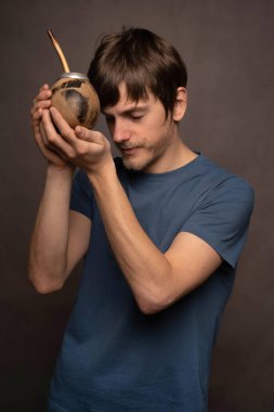 Kahverengi saçlı, uzun boylu, zayıf beyaz bir adam gri arka planda mavi gömlekli, eşine tapıyor.