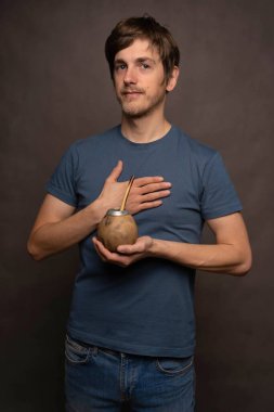 Genç yakışıklı, uzun boylu, zayıf, kahverengi saçlı, mat bardağı tutan, göğsünde gri arka planda mavi gömleği olan beyaz bir adam.