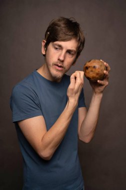 Genç yakışıklı, uzun boylu, zayıf, kahverengi saçlı, düşünceli, gri arka planda mavi gömlekli, beyaz bir adam.