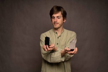 Genç yakışıklı, uzun boylu, zayıf, kahverengi saçlı, elinde siyah beyaz kristaller olan beyaz adam gri arka plandaki çizgili gömlekle onları yargılıyor.