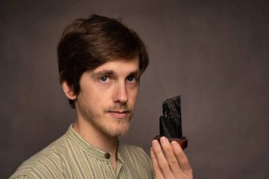 Genç, uzun boylu, zayıf, kahverengi saçlı, siyah kristalli, gri arka planda çizgili gömleği olan, yakışıklı, beyaz bir adam.