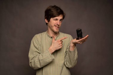 Genç yakışıklı, uzun boylu, zayıf, kahverengi saçlı, gri arka planda siyah kristale göz kırpan beyaz bir adam.