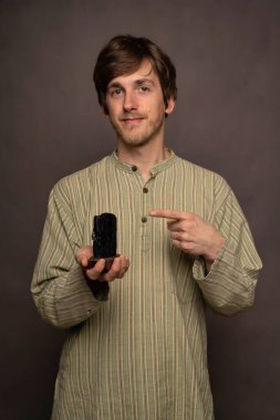 Genç, uzun boylu, zayıf, kahverengi saçlı, gri arkaplanda siyah kristali gösteren beyaz bir adam.