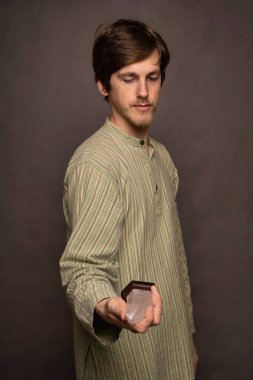 Genç yakışıklı, uzun boylu, zayıf, kahverengi saçlı, gri arka planda çizgili gömlekli, kristal tutan beyaz bir adam.